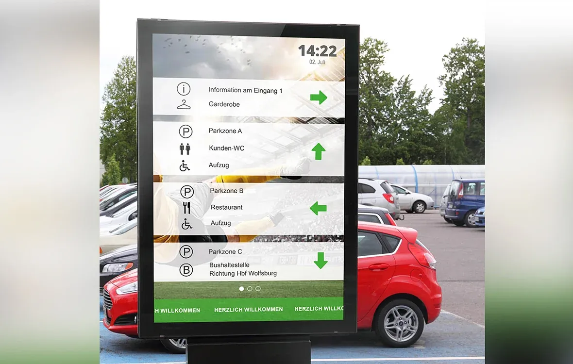 Digitaler Informationsbildschirm auf einem Parkplatz, der Wegbeschreibungen zu Eingängen, Parkzonen, Toiletten und Restaurants anzeigt.