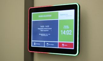 Digitales Türschild mit LED-Farbanzeige zur Anzeige der aktuellen Raumbelegung und verbleibenden Meeting-Dauer. Das Display zeigt eine Raumreservierung für „Raum Aquarium“ mit einer Uhrzeit- und Terminübersicht.