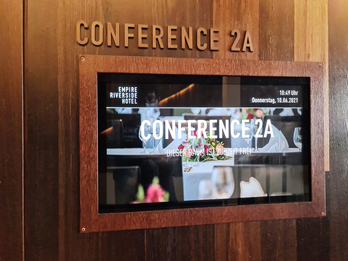 Digitaler Begrüßungsbildschirm im Empire Riverside Hotel zeigt den Status des Konferenzraums 2A mit aktuellen Veranstaltungsinformationen.