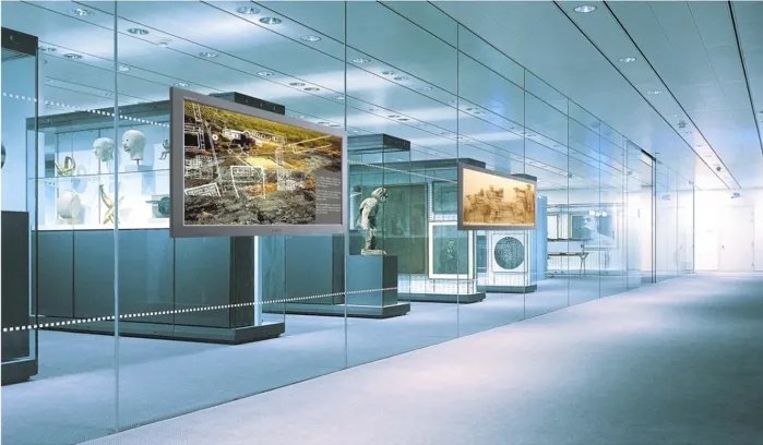 Digital Signage Infoboards in einem modernen Museum präsentieren historische Inhalte und interaktive Informationen in einer hochwertigen, gläsernen Ausstellungsumgebung.